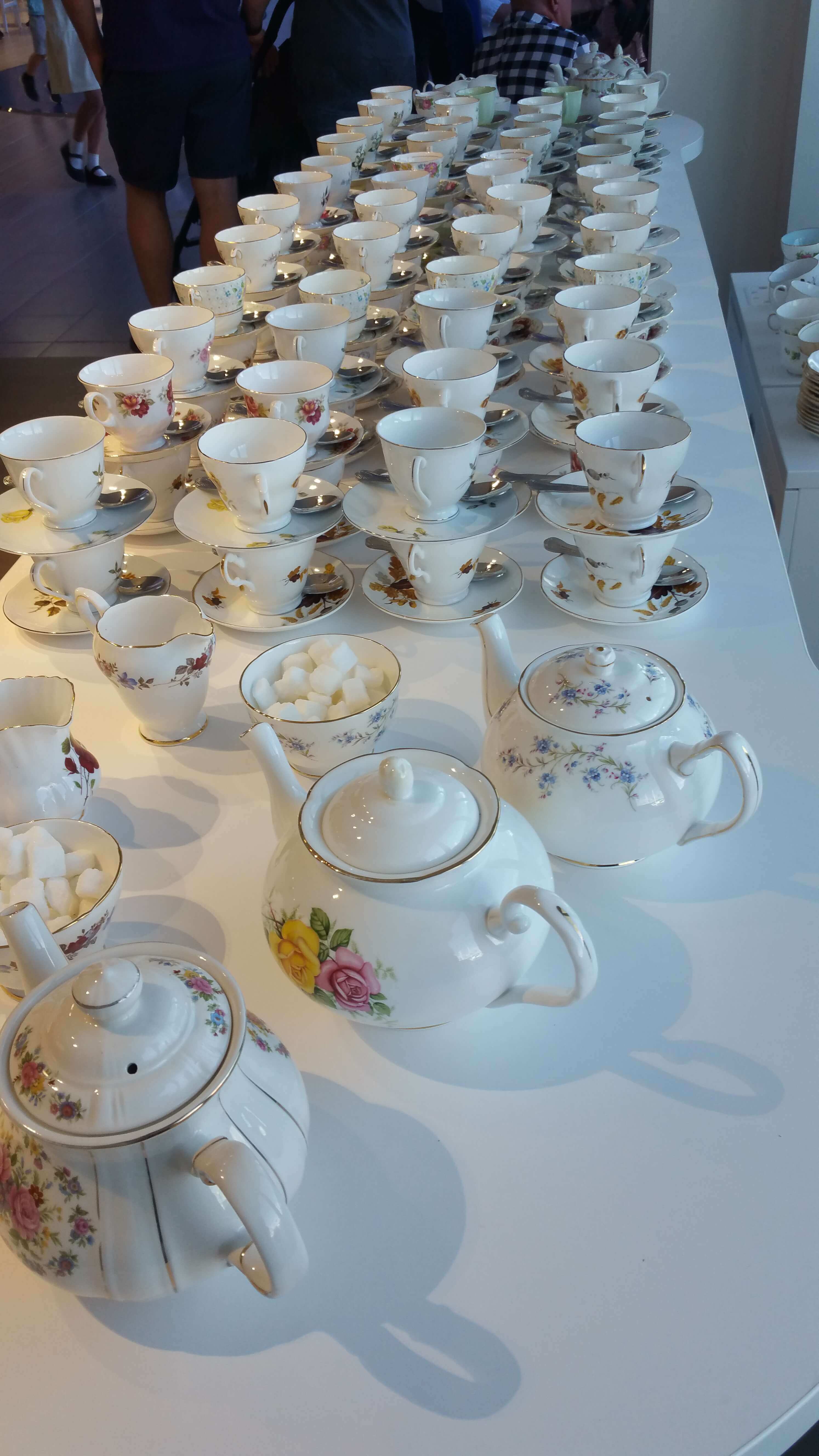 Photo shows vintage tea cups and tea pots lined up ready for tea to be served