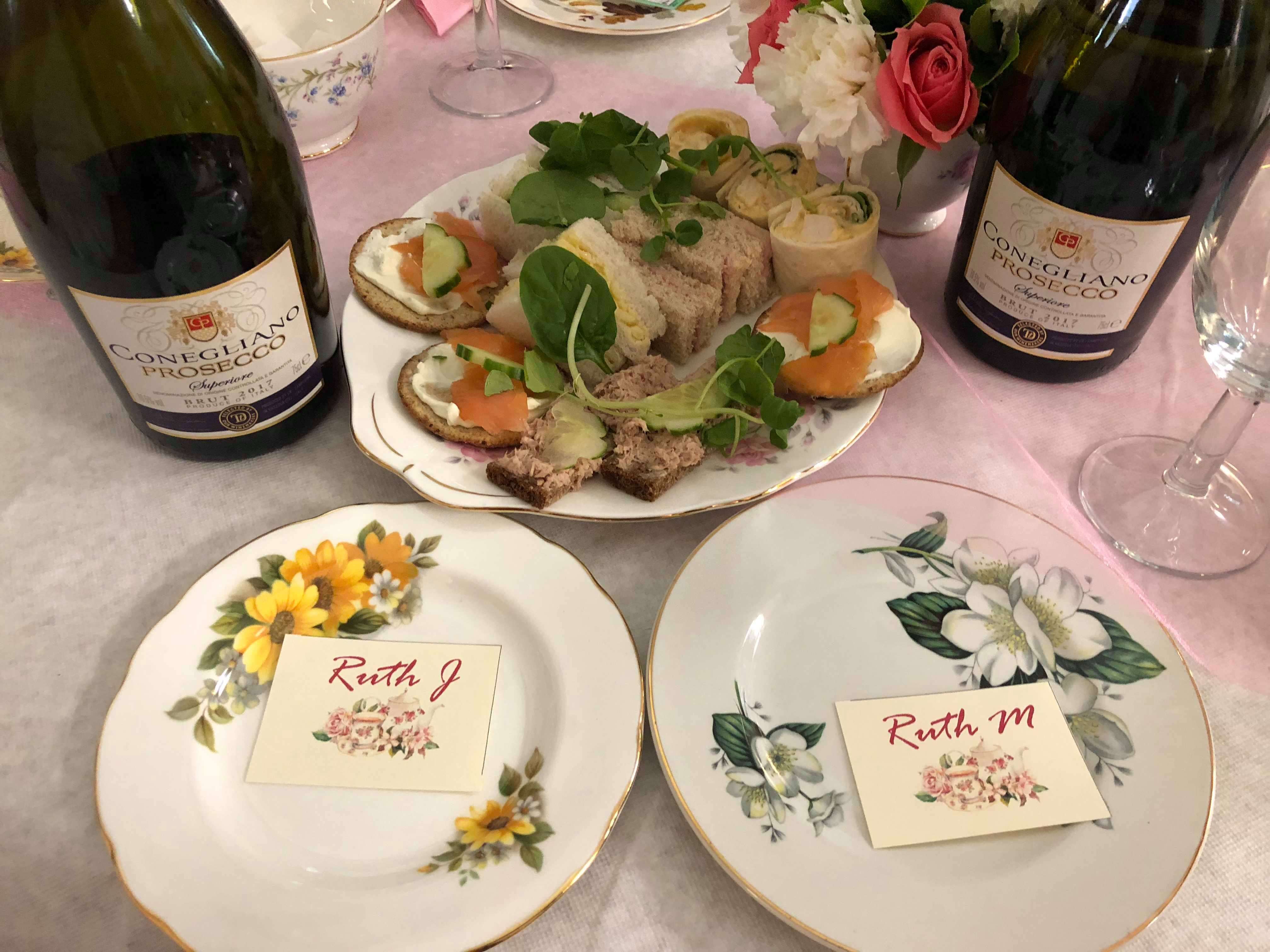 Photo shows dainty sandwiches and bottles of Prosecco amongst vintage china at a Tea Party